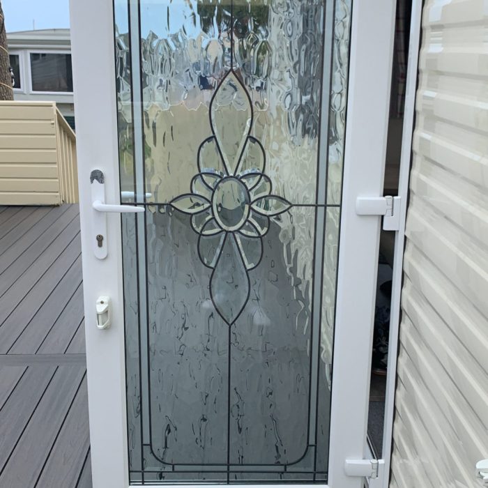 White door with stained glass featuring a floral design, opening to a deck with wooden flooring and a palm tree in the backgr
