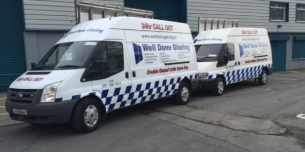 Two branded vans for Welldone Glazing parked outside a building, featuring blue and white checkered designs and service detai
